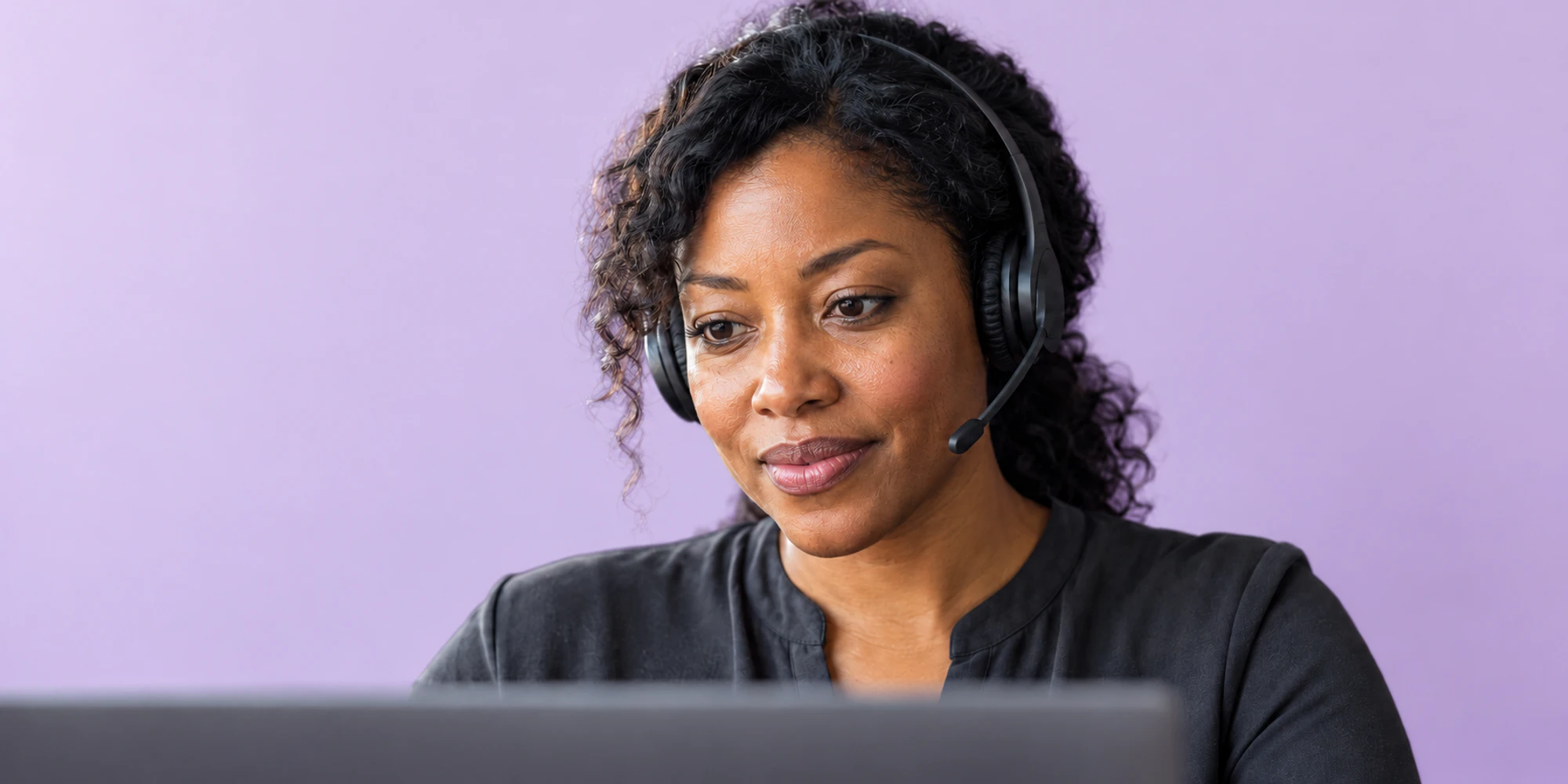 A customer support specialist focuses on a conversation with a headset against a lavender background